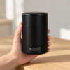 Hand holding the Kokuyō Chazutsu matte black tea canister on an oak table